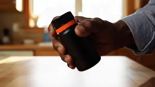 Hand shaking a small dark bottle three times over a wooden counter and twisting the cap